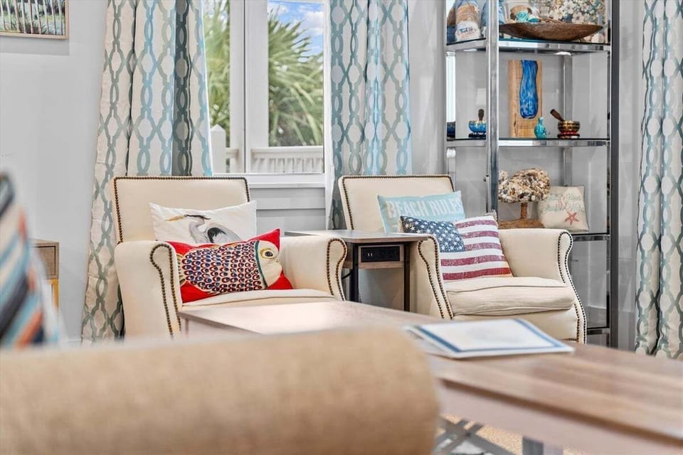 Cozy living room seating nook with accent chairs, decorative shelving, and coastal-inspired décor throughout.