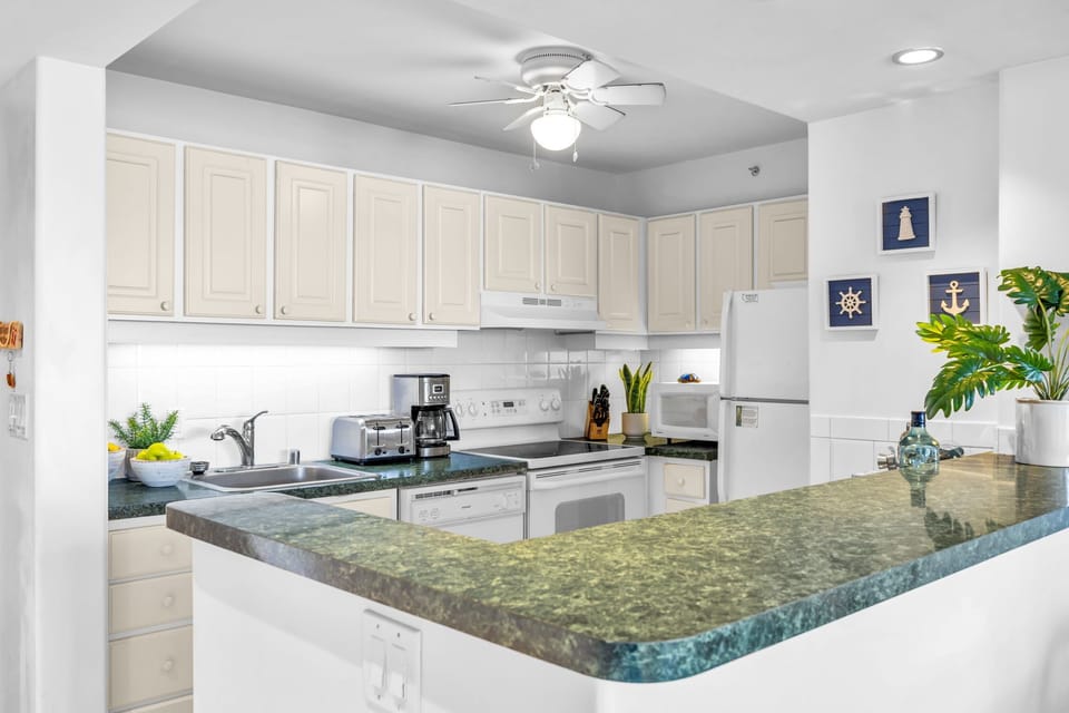 Prepare meals with ease in a well‑equipped kitchen featuring ample storage, bright lighting, and green‑toned countertops that add a warm island touch.