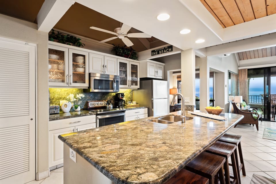 Bright kitchen with granite countertops, stainless steel appliances, and large windows overlooking tropical greenery