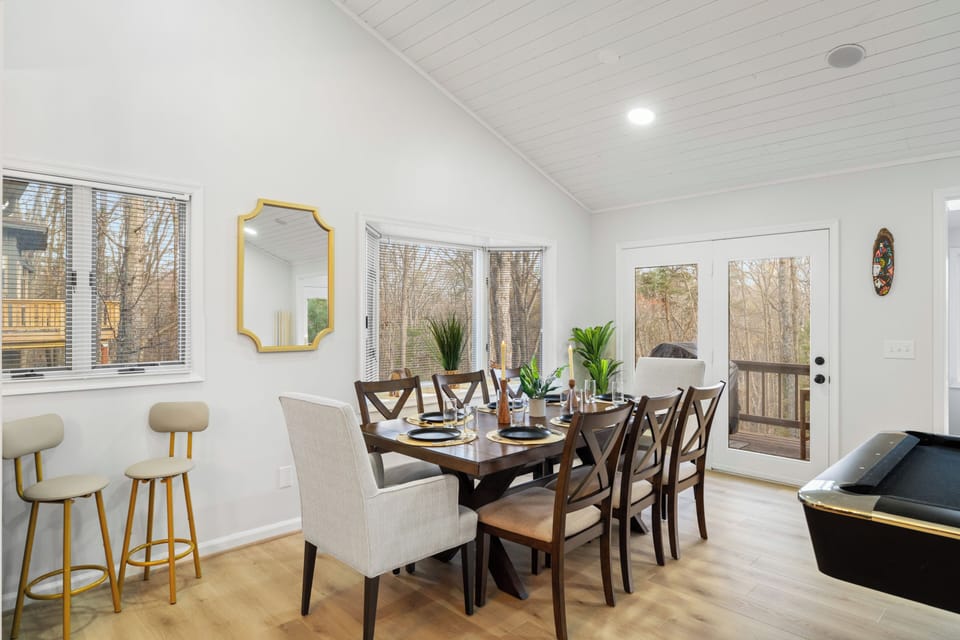 Sunny dining room with forest views, deck access, and game table.