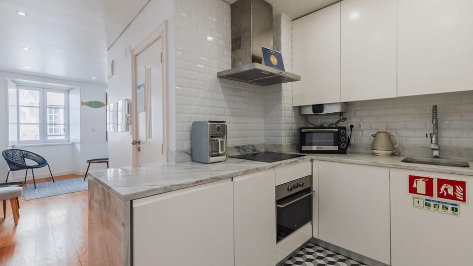 A compact kitchen with sleek white finishes, marble countertops, and all the essentials for a comfortable stay. #EffortlessCooking #ModernLiving