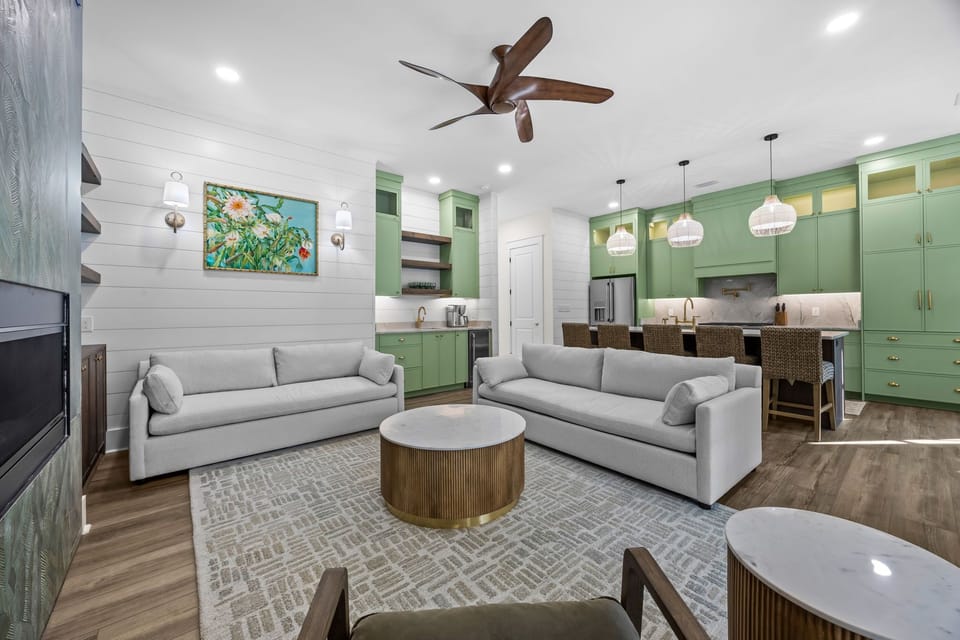 An elegant coastal living space with custom green cabinetry, warm wood tones, and tailored furnishings, anchored by a refined kitchen and open layout—thoughtfully designed for comfort, conversation, and effortless indoor-outdoor flow.