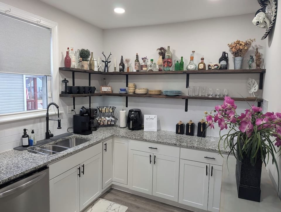 A bright, modern kitchen with granite counters, stainless appliances including a large double door fridge-freezer combo, and a fully stocked coffee bar. Laundry room and direct access to the backyard make this space flow for those on the go!