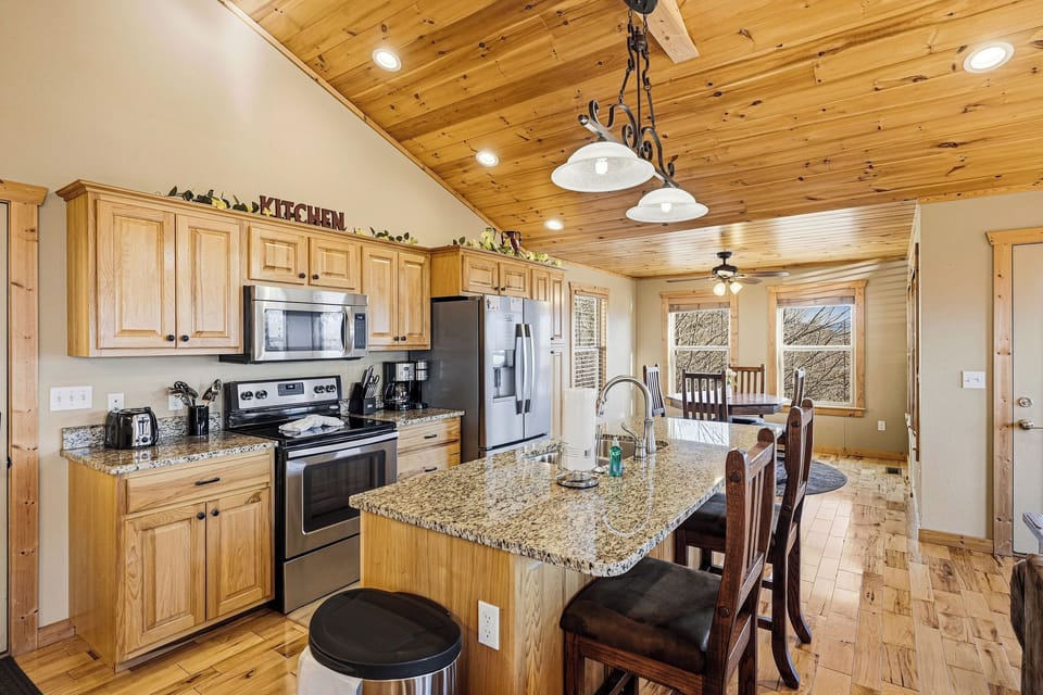 Your fully-equipped kitchen awaits with granite counters, stainless appliances, and rustic wood ceilings—perfect for cooking memorable meals together.