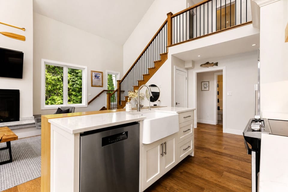 Open-concept kitchen and living space featuring soaring ceilings, a large island with farmhouse sink, and warm modern finishes throughout.