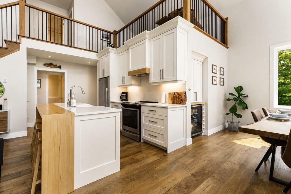 Bright open-concept kitchen and dining area featuring soaring ceilings, modern finishes, and a spacious island — designed for gathering, entertaining, and effortless cottage living.