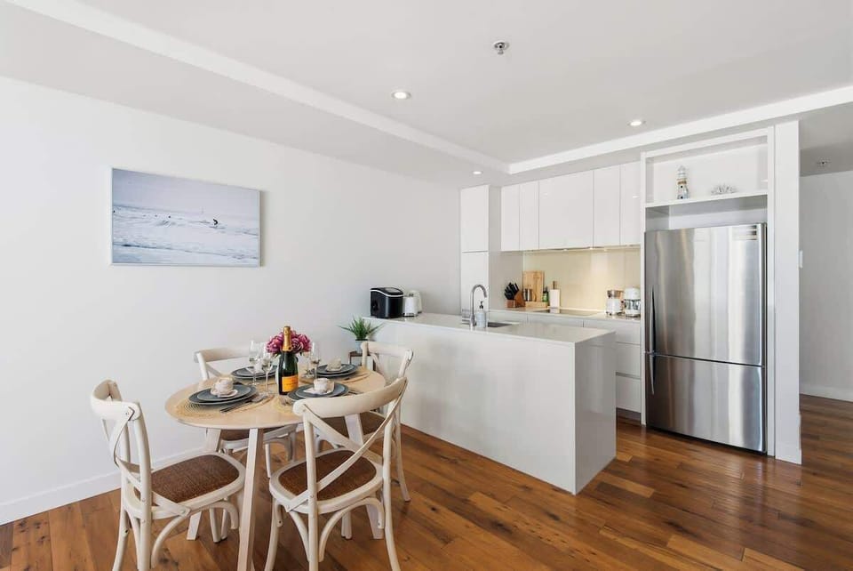 Kitchen and dining area with white cabinetry, round wooden table set for four and bright atmosphere creating a welcoming space for meals.