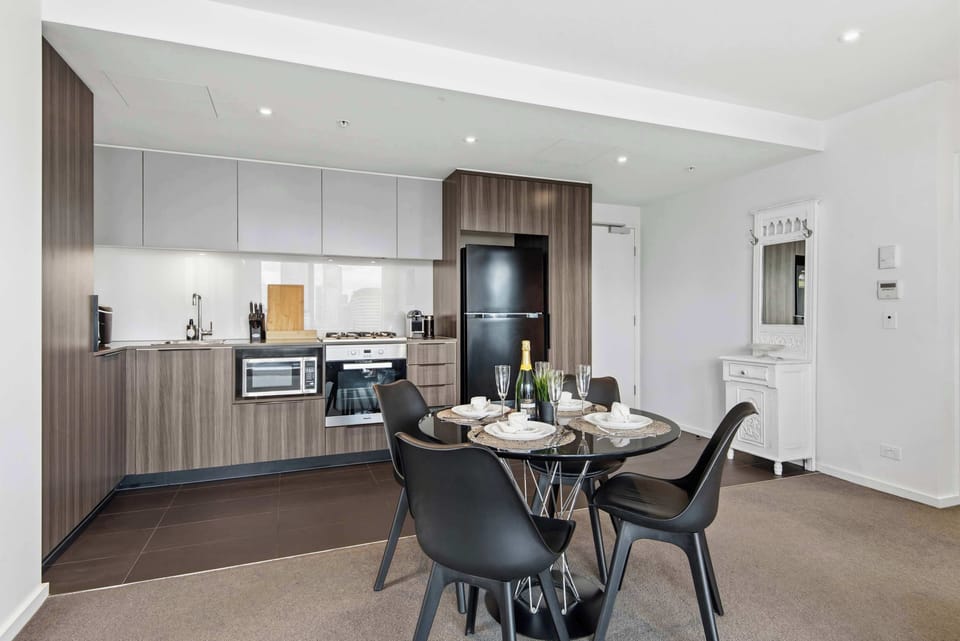 Kitchen with wood‑paneled cabinets, glass dining table and modern appliances creating a contemporary and inviting space.