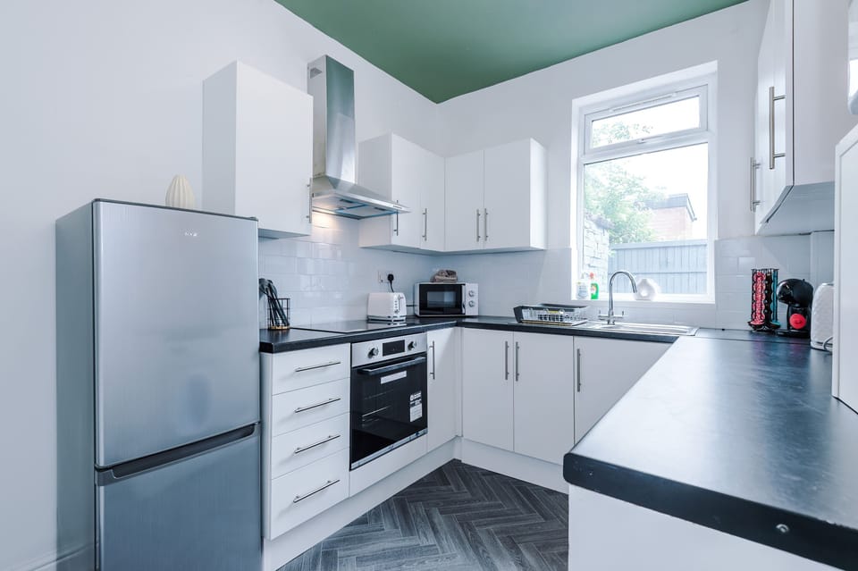 Bright, modern kitchen with white cabinets, dark countertops, and sleek appliances. Includes a washing machine, stainless steel sink, and wall-mounted boiler, a functional, well-lit space ideal for cooking and laundry convenience during your stay.