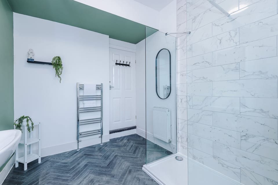 Modern bathroom with a glass-enclosed shower, marble-patterned walls, and sleek fixtures. Includes a toilet, sink, and large window for natural light , bright, minimalist space designed for comfort and style.