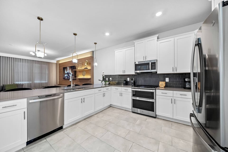 Welcome to this stylish kitchen featuring sleek white cabinetry and a striking dark backsplash. Bright lighting and spacious countertops inspire your culinary creativity, while modern appliances make meal prep effortless.