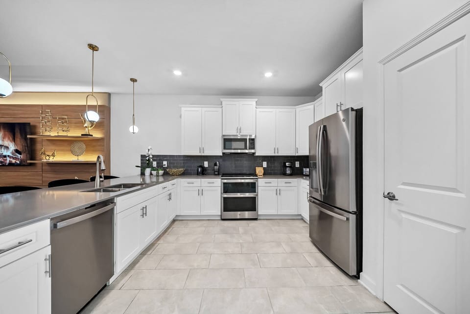 Welcome to a sleek kitchen featuring glossy white cabinetry and rich dark countertops. With contemporary fixtures and stainless steel appliances, it's an efficient space perfect for meal prep and casual gatherings.