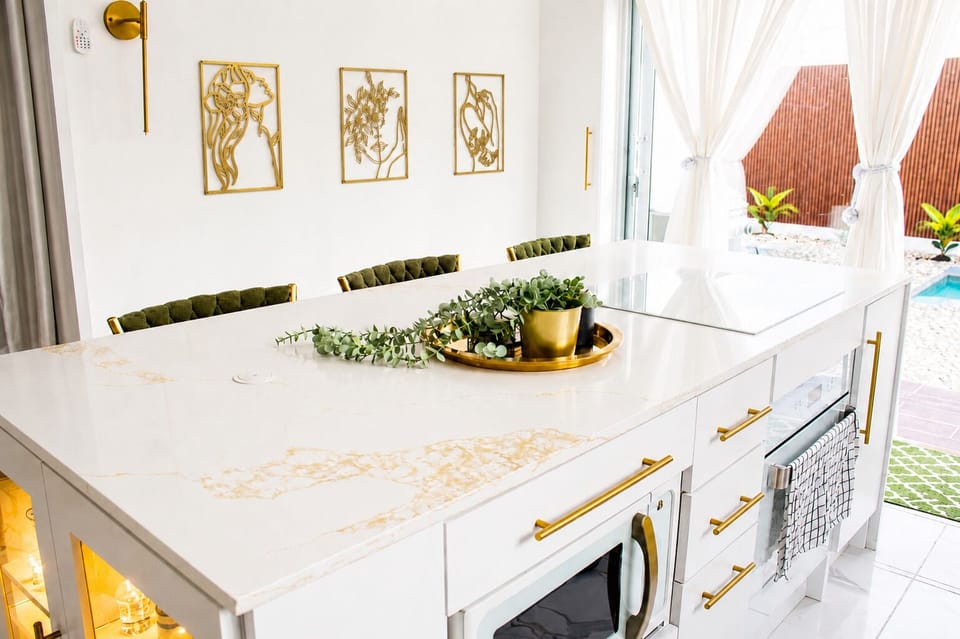 Bright modern kitchen with marble island, gold accents & pool views.