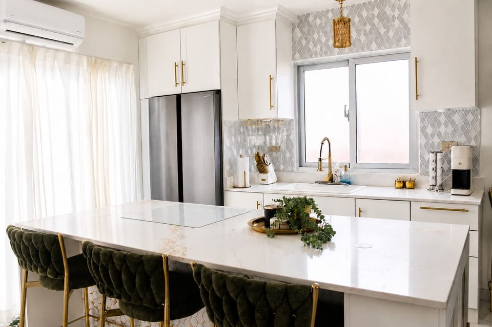 Bright modern kitchen with marble island, velvet stools, and gold accents.