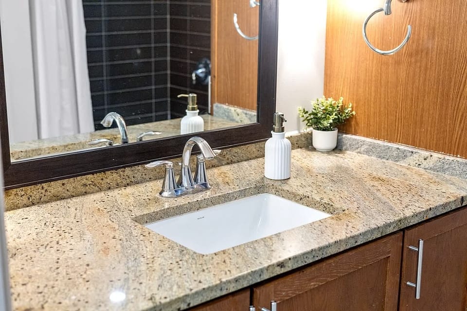 Bright bathroom vanity with granite countertop, modern sink, and ample lighting. Stocked with essentials and styled for comfort, providing a clean and organized space for your stay.