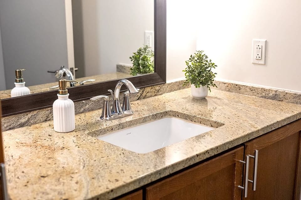 Spacious bathroom vanity with granite countertop, modern sink, and ample lighting. Clean and well maintained with essential toiletries provided, offering a comfortable setup for daily routines during your stay.