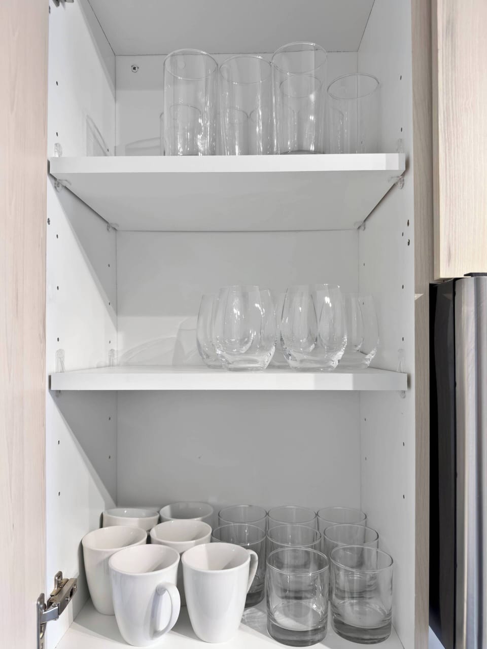 A well-stocked kitchen shelf displaying glassware and coffee mugs. This functional and stylish display ensures you have easy access to essential drinkware for enjoying your favorite beverages.