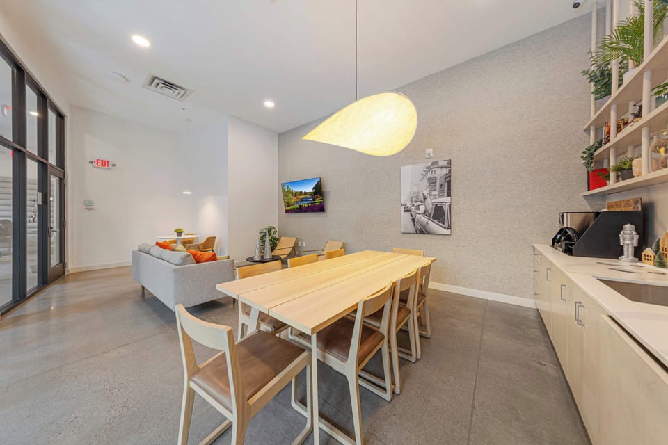 A modern event room with a spacious dining table and contemporary lighting. The clean design and ample seating make it an ideal space for meetings, social events, or group gatherings, with a welcoming atmosphere for all.