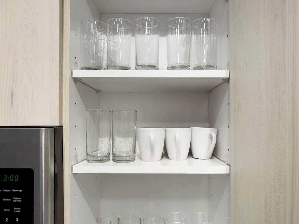 A clean and organized shelving unit stocked with glasses and other kitchen essentials. The space is designed to keep everything neatly in place, ensuring a smooth and enjoyable stay with easy access to your drinkware.