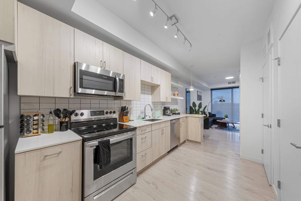 A well-lit kitchen featuring high-quality appliances, including a microwave, oven, and stovetop. The light wood cabinetry and sleek design provide a stylish and functional space for all your cooking needs.