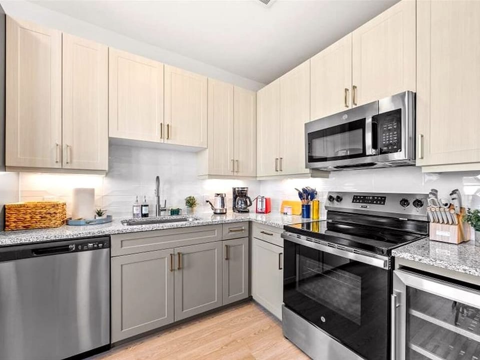 Modern kitchen with stainless-steel appliances, granite countertops, and sleek cabinetry. Fully equipped with stove, oven, microwave, dishwasher, and essentials like coffee maker, toaster, and utensils for easy home-style dining.