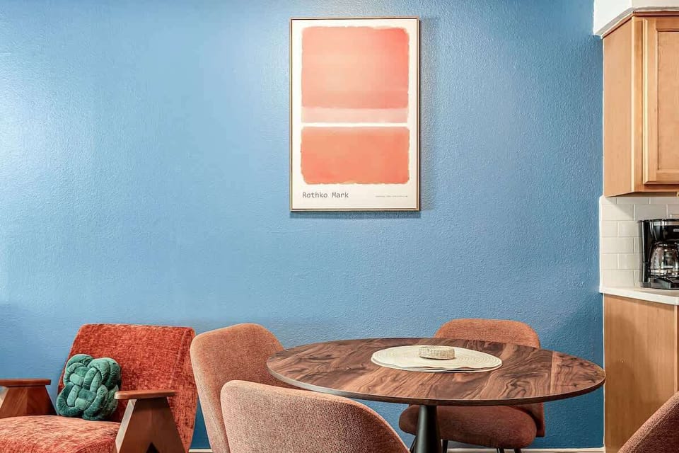Stylish dining nook framed by bold blue walls, mid-century chairs, and abstract art — a chic spot for morning coffee or dinner chats.
