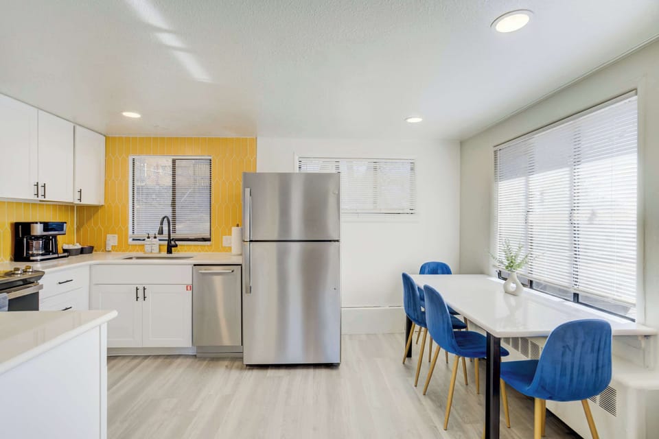 The fully stocked kitchen is equipped with stainless steel appliances, a unique yellow accent wall, and white cabinetry. A breakfast bar with stylish blue velvet stools provides a convenient spot for morning coffee or a quick bite.