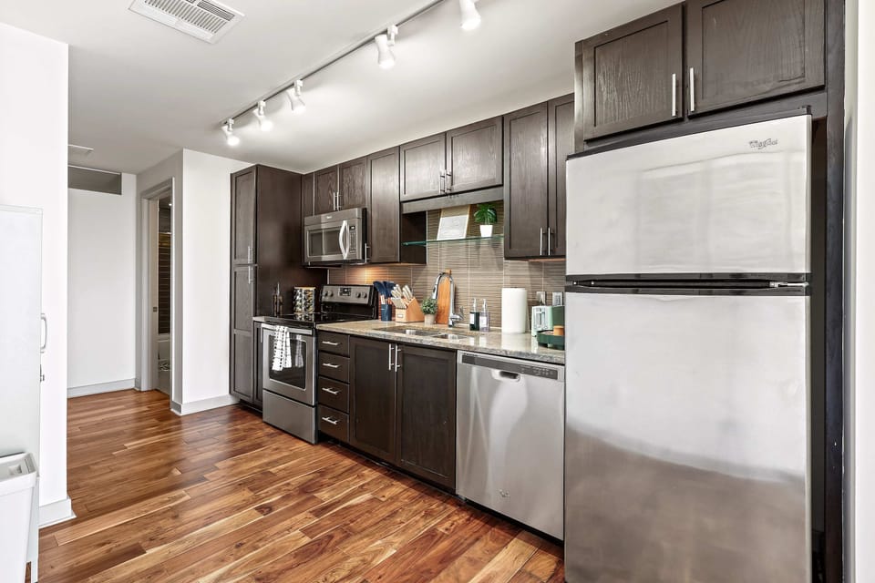 Step into this sleek, modern kitchen featuring rich dark cabinetry, stainless steel appliances, and warm wood floors. Fully equipped and thoughtfully laid out, it’s perfect for cooking, entertaining, and enjoying meals with ease and style. ✨🍽️
