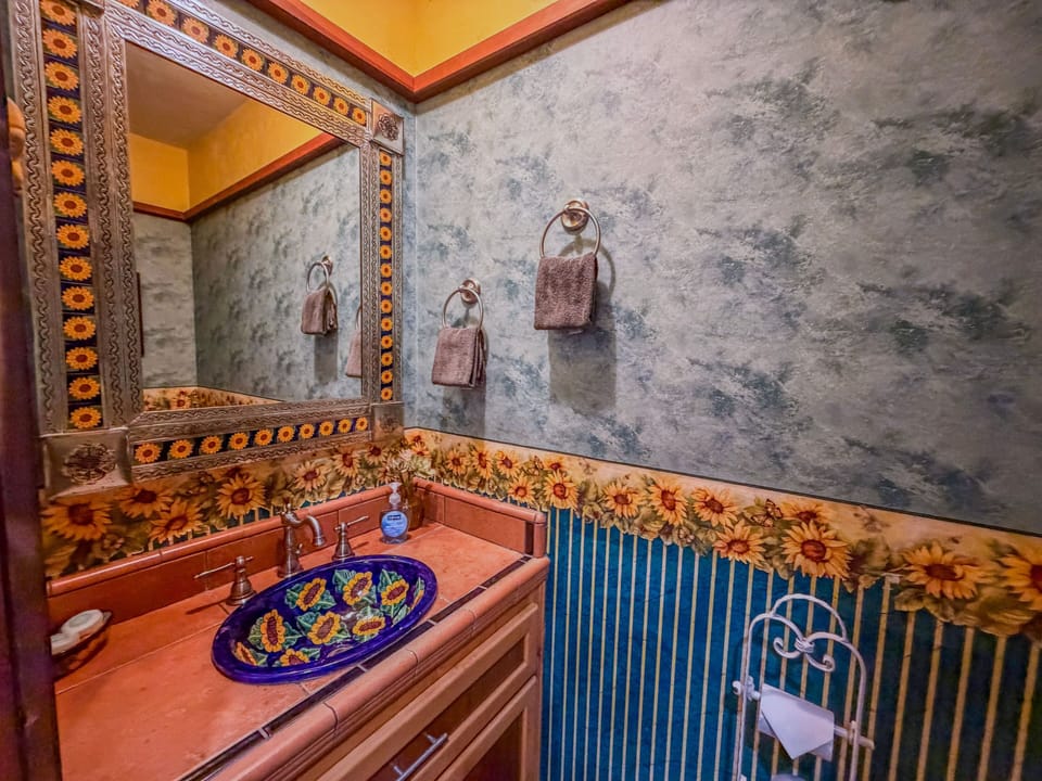 Bathroom vanity with sunflower-themed tilework, mirror frame, and painted sink.
