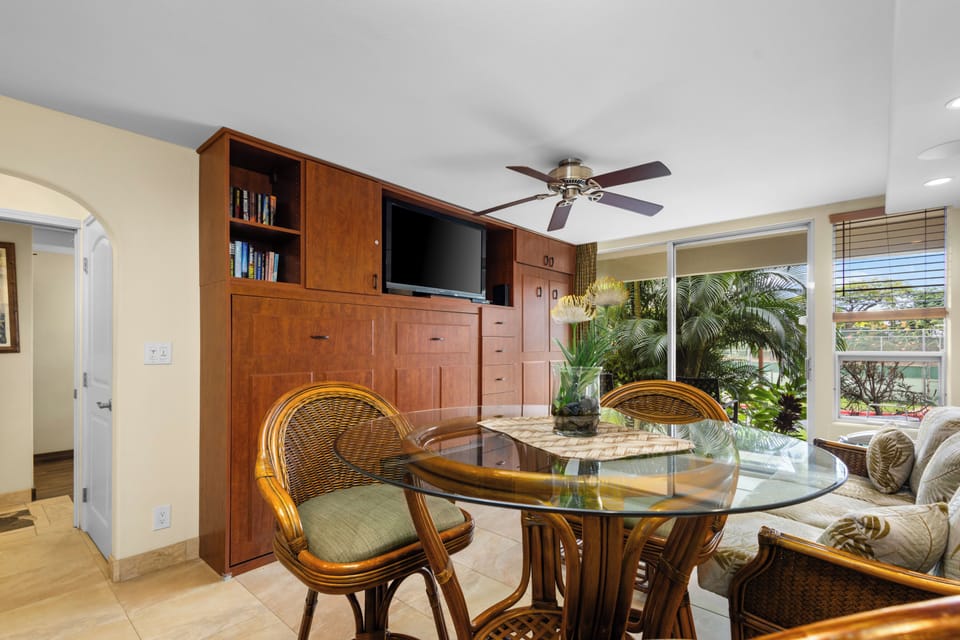 Relax in your tropical-themed living space with beautiful built-in storage, dining nook, and lush plants creating a serene indoor oasis.