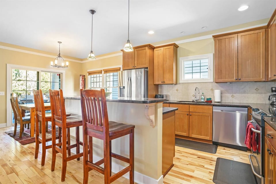 Open kitchen with stainless appliances, spacious countertops, and a large island with bar seating – flowing into a sunny dining area perfect for family meals.