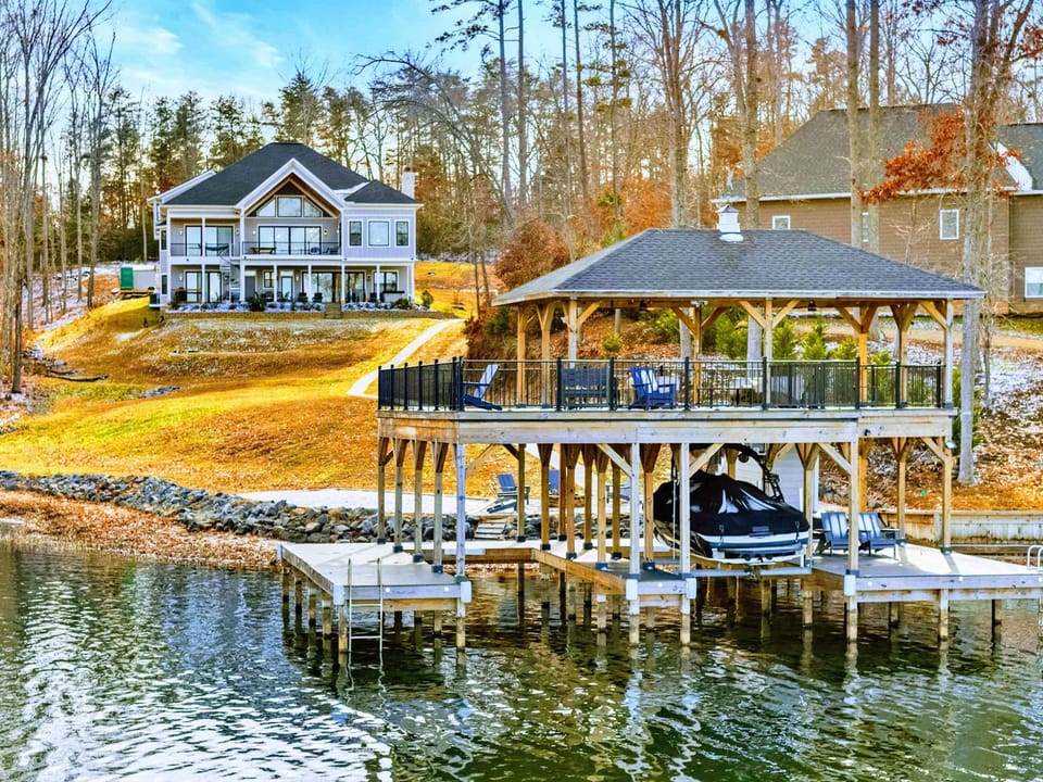 Lakefront Exterior - A wide-angle view of the home from the lake, showing the wraparound deck, balcony, and wooded lot.