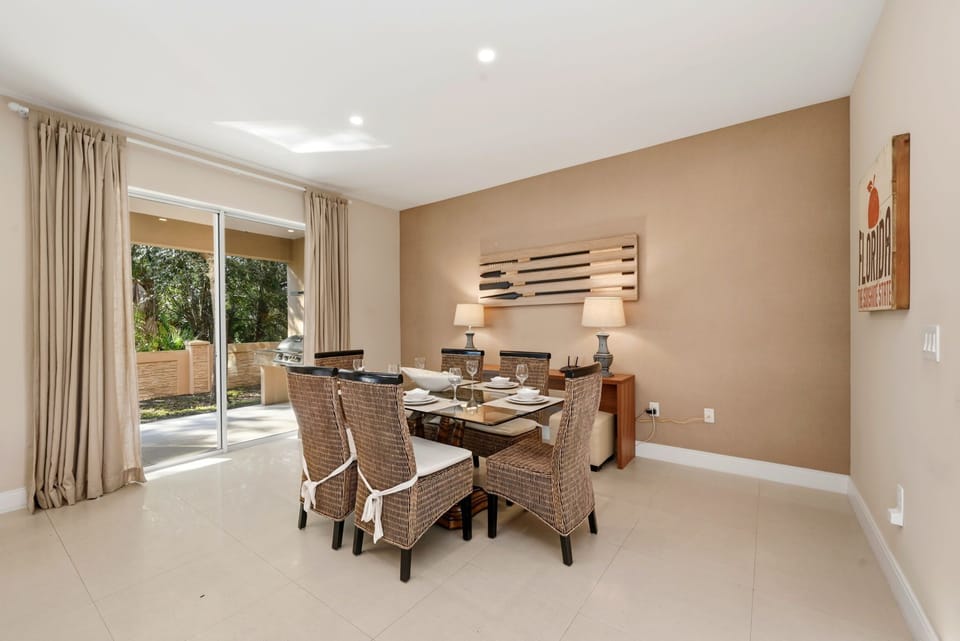 Dining area with wicker chairs and sliding doors opening to a patio with garden views