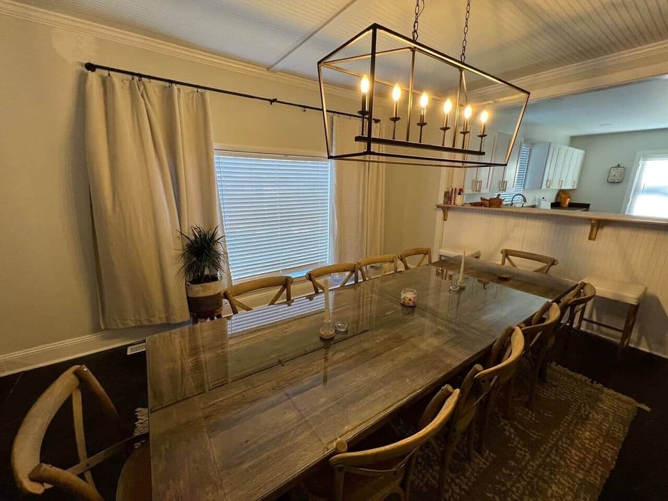 This elegant dining area features a table with six comfortable chairs, perfect for family meals or dinner parties. The space is beautifully lit with six overhead bulbs, and the large window offers a lovely view while you dine.