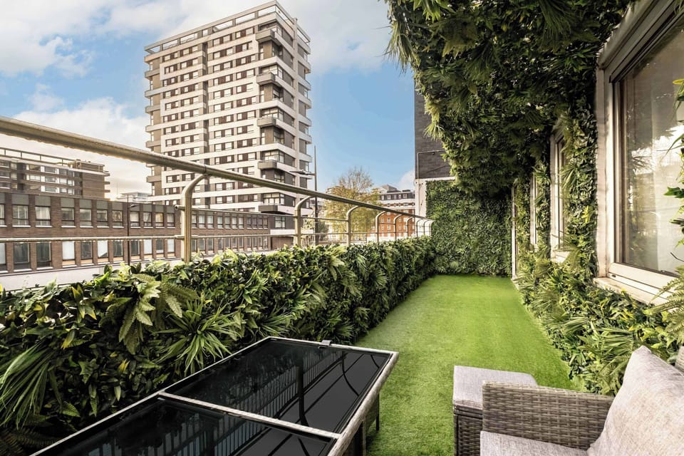 Balcony | A beautiful balcony with an outdoor seating area for comfort and cosiness, surrounded by lush wall plants throughout, creating a relaxing and charming atmosphere.