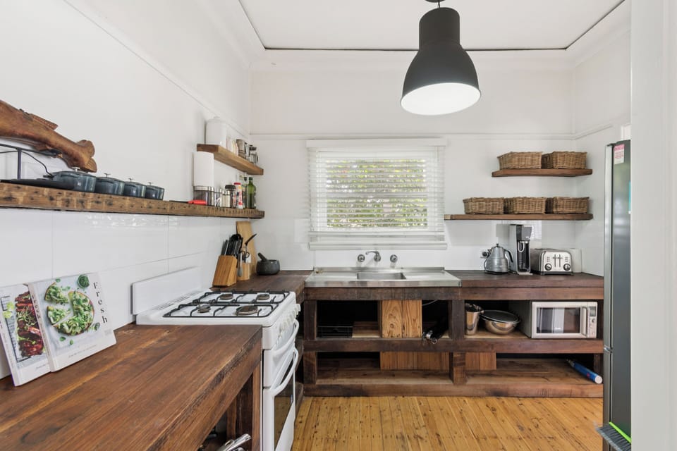 Cook with ease in the thoughtfully equipped kitchen featuring handcrafted wooden benchtops, open shelving, and all the essentials for home-style meals, including a gas stove, kettle, and microwave.