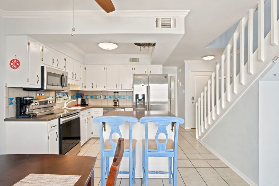 Your bright, fully-equipped kitchen invites you to whip up morning coffee or a family meal. Notice the island seating, stainless appliances, and cheerful coastal touches that make this space feel both practical and welcoming.