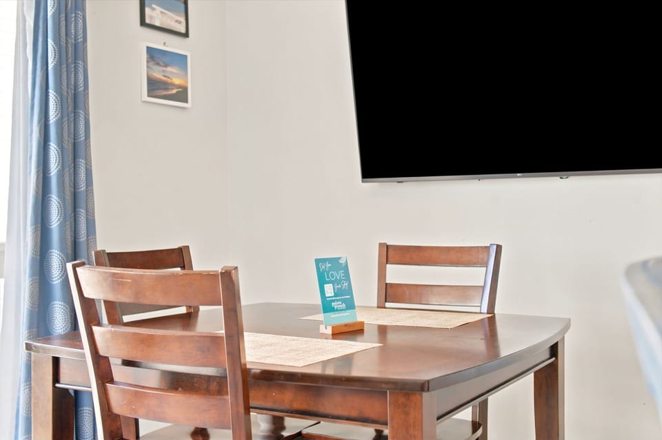 Your cozy dining area invites you to share meals together beneath warm natural light, with a flat-screen TV ready for entertainment and cheerful wall art to brighten your stay.