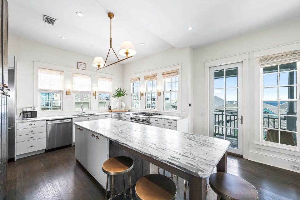 Cook with ease in this bright, modern kitchen featuring marble counters, stainless appliances, and stunning water views through floor-to-ceiling windows.