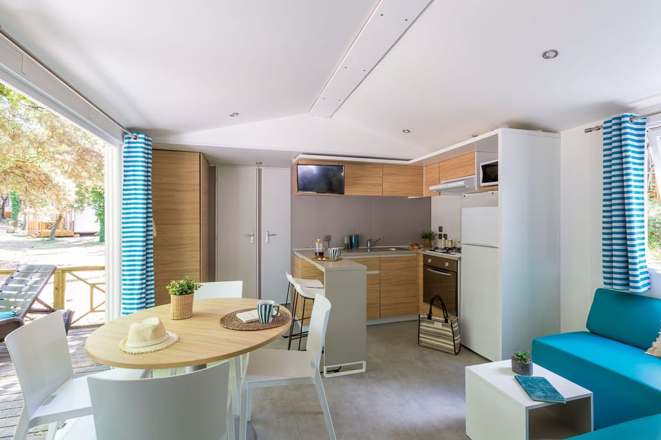 The airy living area features a cozy couch and dining space, complemented by large windows that provide natural light and views of the lush landscape.
