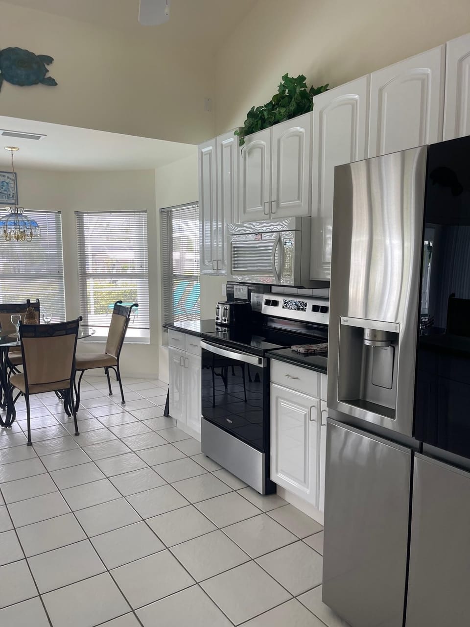 Kitchen from alternate angle showing stainless refrigerator, range, and cabinetry with tile flooring