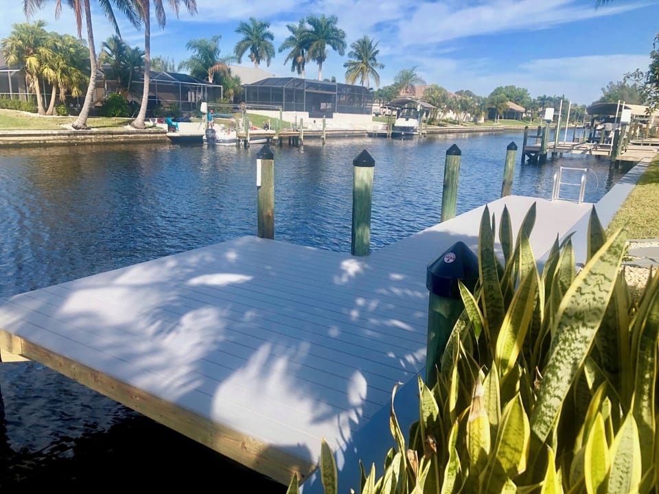 Canal waterway with dock pilings, tropical landscaping, and open water views