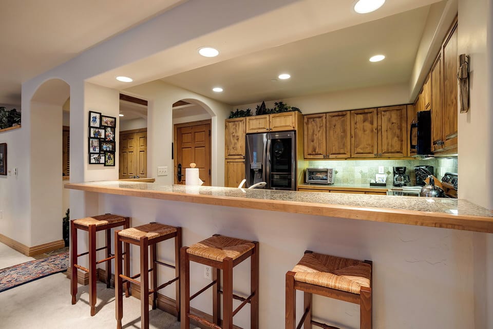 Gather around this spacious kitchen bar where warm wood tones and granite counters create the perfect spot for your morning coffee or evening conversations.
