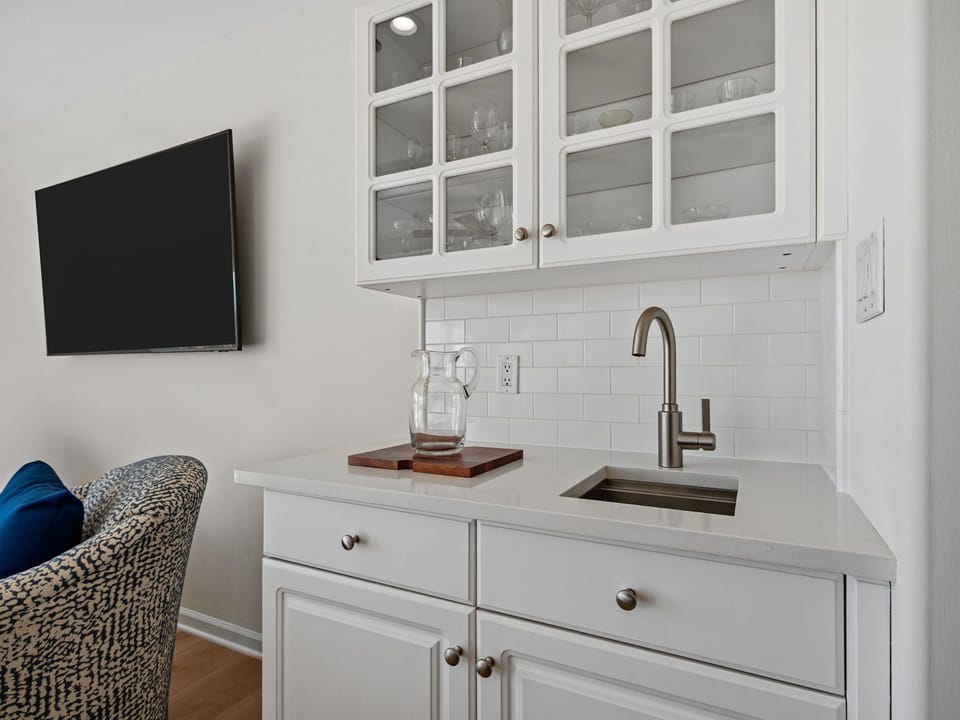 Your elegant wet bar features white cabinetry, subway tile backsplash, and modern appliances for convenient meal prep.