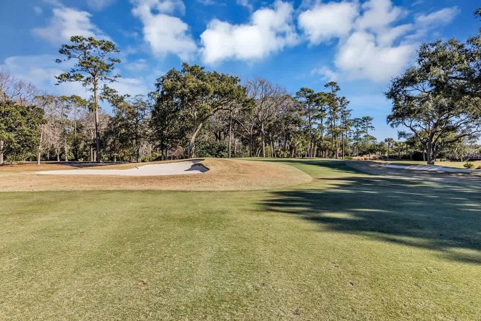 Championship golf course featuring manicured fairways and sand bunkers surrounded by mature oak trees under bright blue skies.