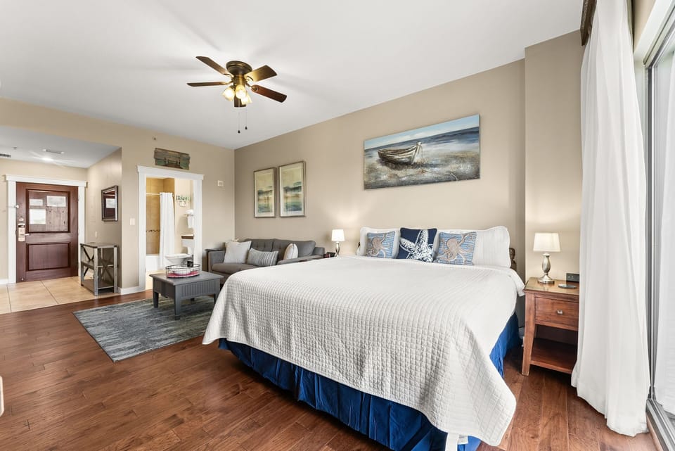 Relax in your spacious coastal-themed bedroom with nautical artwork, comfortable seating area, and modern amenities creating the perfect vacation retreat.