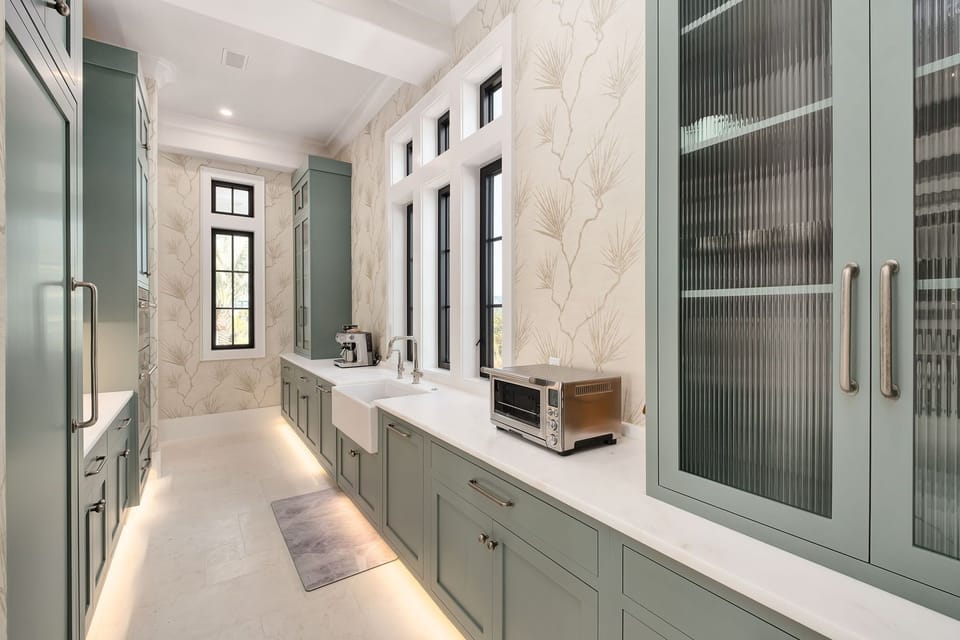 Step into this elegant galley kitchen where sage-green cabinetry and botanical wallpaper create a serene cooking space with modern amenities at your fingertips.