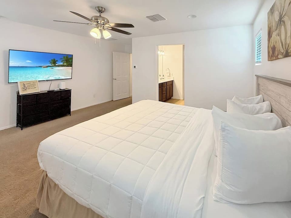 Bedroom with bed, TV on dresser, chair, ceiling fan, and bathroom doorway