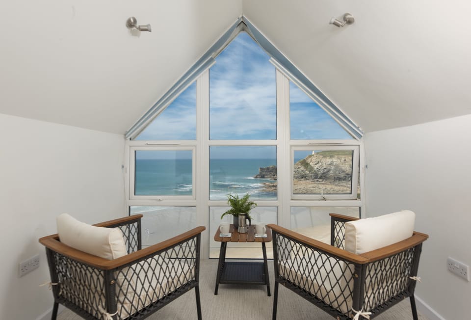 Seaside House, Portreath. Master bedroom with a feature window and seating area framing sweeping sea views