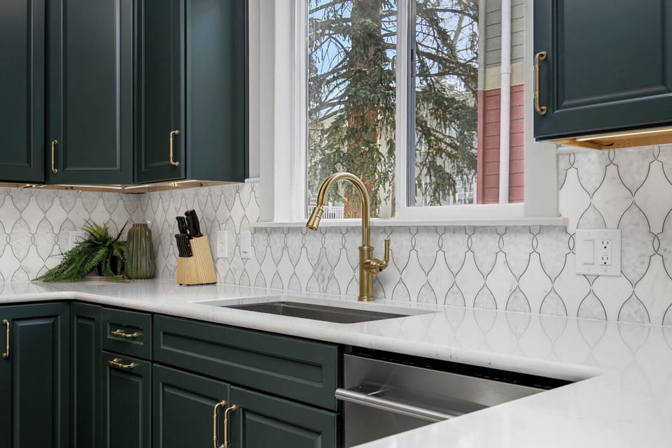 Your stylish kitchen features elegant green cabinets, brass fixtures, and geometric tile backsplash for memorable meal preparations.